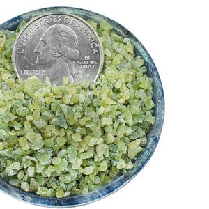 以下が含まれることがあります： 小さな青い縁の丸いボウルに、小さな薄緑色の不規則な形の石が敷き詰められ、その中に銀色の25セント硬貨が置かれています。硬貨には人物の横顔が描かれています。