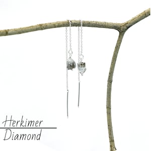 Könnte beinhalten: Silberne Ohrringe mit einem rohen Herkimer-Diamantenkristall an jedem Ohrring. Die Ohrringe hängen an einem Zweig.