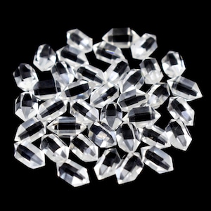 May include: A collection of numerous small, clear, double-terminated quartz crystals. Each individual piece features a hexagonal, faceted shape with pointed ends, displaying a transparent, glass-like appearance scattered across the frame.