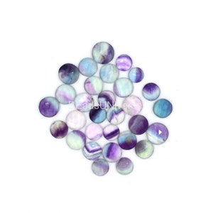 May include: A collection of round, polished fluorite stones in shades of purple, blue, and white. The stones are arranged in a loose pile on a white background.