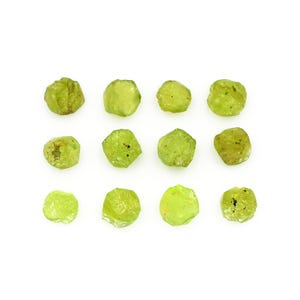 Puede incluir: Doce piedras preciosas de peridoto en bruto, de color verde claro, se muestran sobre un fondo blanco. Las piedras tienen una textura natural y rugosa y formas irregulares. El color varía de verde pálido a un verde oliva ligeramente más oscuro.