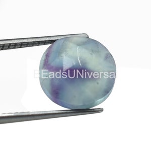 May include: A round, light blue fluorite gemstone with purple and white streaks. The gemstone is held by a pair of tweezers.