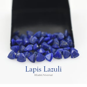May include: A close-up of a pile of triangular lapis lazuli gemstones. The stones are a deep blue colour with flecks of gold pyrite. The stones are spilling out of a black velvet box. The text "Lapis Lazuli" and "BeadsUniversal" is visible below the stones.