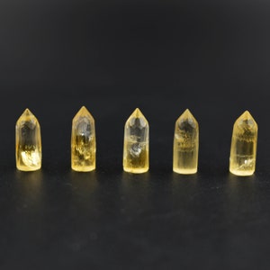 May include: Five clear, yellow crystal points arranged in a row on a black surface. The points are all the same size and shape, and they are all pointed at the top.