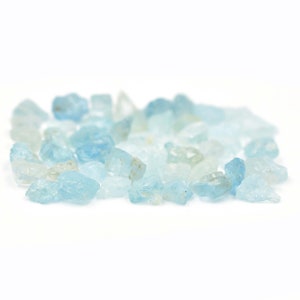 May include: A pile of light blue aquamarine gemstones, some with a more opaque white color, are scattered on a white background.