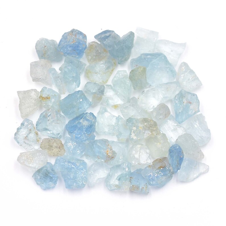 May include: A collection of light blue aquamarine rough stones. The stones are various sizes and shapes, with some having a more opaque appearance than others.
