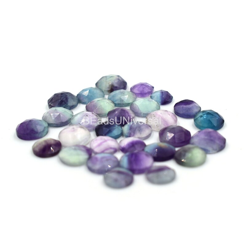 May include: A collection of 20 faceted fluorite gemstone cabochons in shades of purple, green, and blue. The cabochons are approximately 10mm in diameter.