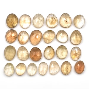 May include: Twenty-four faceted, oval-shaped, translucent gemstones in shades of light brown and yellow. The stones are arranged in four rows of six stones each.