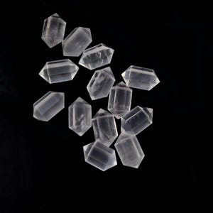 May include: A collection of twelve clear, double-terminated quartz crystals arranged in a scattered pattern. Each individual crystal features a hexagonal prism shape with pointed ends on both sides, displaying a translucent, glass-like appearance.