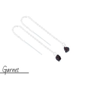 May include: A pair of silver dangle earrings with garnet gemstones. The earrings feature a delicate chain and a small, irregular shaped garnet at the end of each chain.