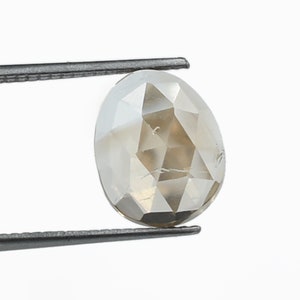 May include: A light brown, oval-shaped, faceted diamond held by tweezers.