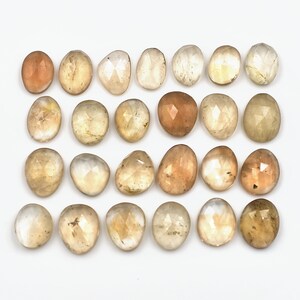 May include: Twenty-four faceted, translucent, light brown gemstones. The stones are oval-shaped and have a smooth, polished finish.