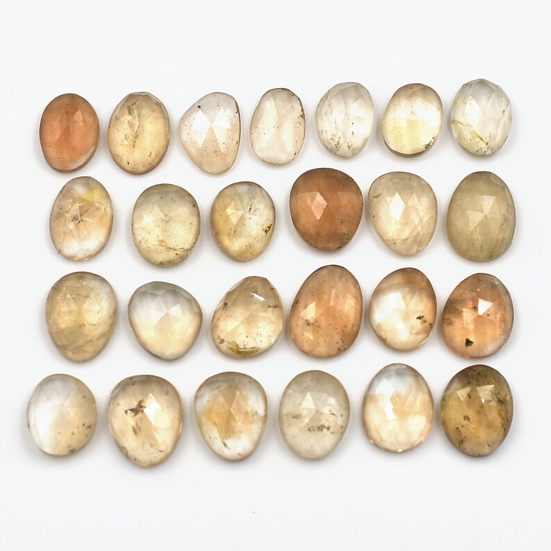 May include: Twenty-four faceted, translucent, light brown gemstones. The stones are oval-shaped and have a smooth, polished finish.
