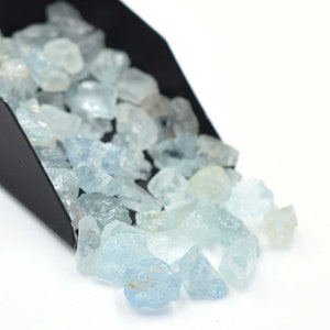 May include: A scoop of light blue aquamarine rough gemstones. The gemstones are various sizes and shapes.