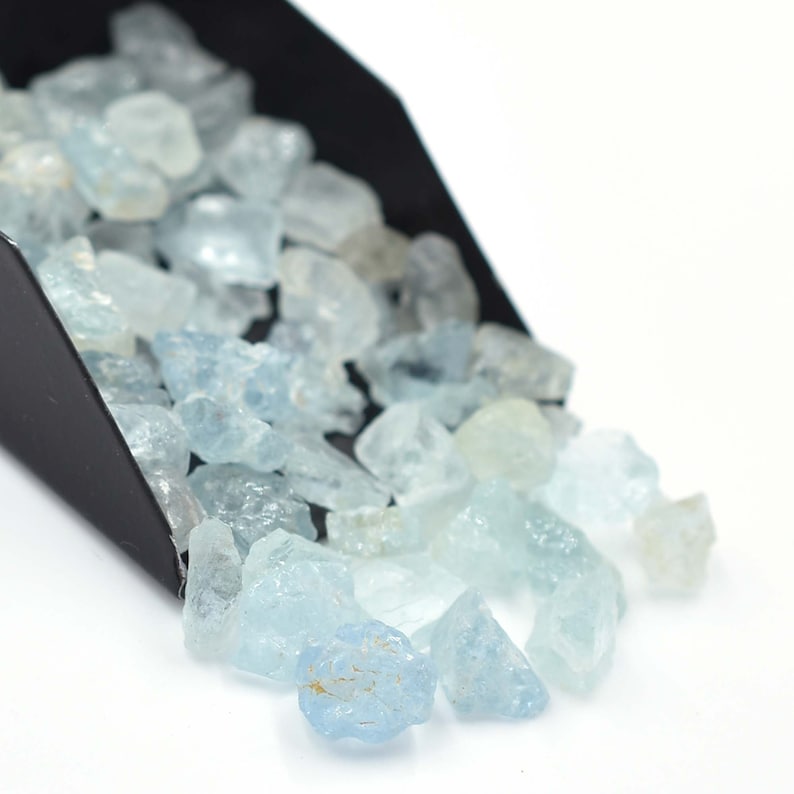 May include: A scoop of light blue aquamarine rough gemstones. The gemstones are various sizes and shapes.