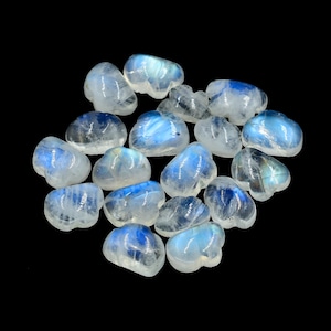 Puede incluir: Una colección de cristales de piedra lunar en forma de corazón. Los cristales son translúcidos y tienen un brillo iridiscente azul.