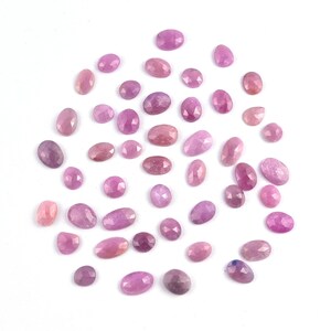 Könnte beinhalten: Eine Ansammlung von rosa und lila Edelsteinen in verschiedenen Formen, darunter oval und facettiert. Die Edelsteine liegen auf einem weißen Hintergrund und zeigen ihre unterschiedlichen Farbtöne und Texturen.