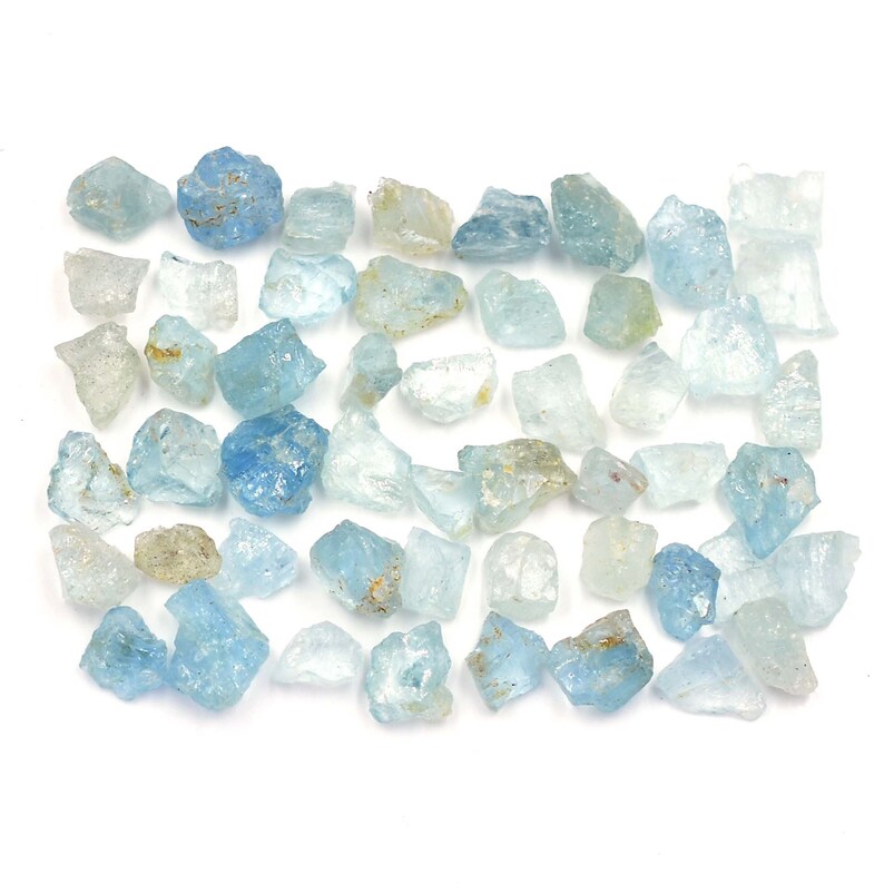 May include: A collection of raw aquamarine crystals in various sizes and shades of blue. The crystals are rough and have a natural, unpolished appearance.