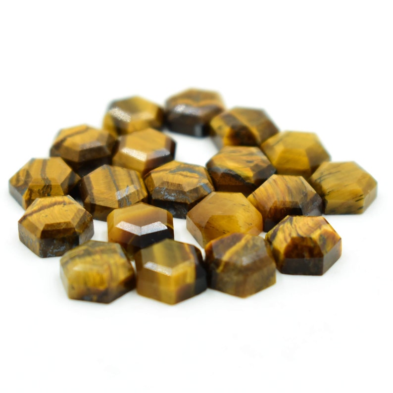 May include: A cluster of faceted, hexagonal tiger's eye gemstones. The stones are a rich, golden-brown with dark brown stripes. The gemstones are arranged on a white background.