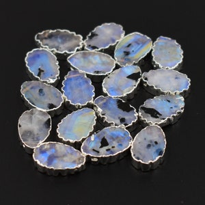 May include: A collection of oval-shaped moonstone beads with a silver-toned edge. The beads have an iridescent blue and white colour.