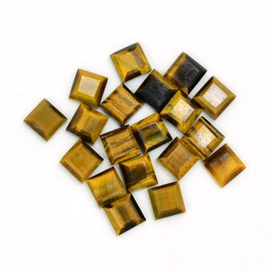 May include: A selection of square-cut tiger's eye gemstones. The stones display a range of golden brown and dark brown hues, with natural patterns. The gemstones are presented on a white background, highlighting their polished facets and unique striations.
