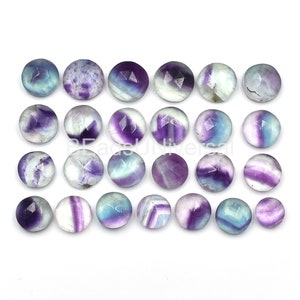 May include: Twenty-four round, faceted fluorite cabochons in shades of purple, blue, and white. The cabochons are approximately 10mm in diameter.