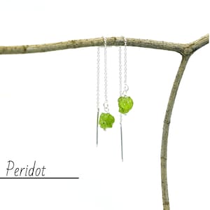 Puede incluir: Un par de pendientes de plata con piedras de peridoto verdes. Los pendientes están colgados de una rama.