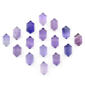 May include: A collection of 16 purple double-pointed crystal wands arranged in a diamond pattern on a white background.