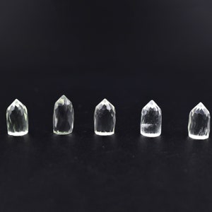 Może przedstawiać: Pięć przezroczystych punktów kryształu kwarcowego, ułożonych w rzędzie na czarnym tle. Kryształy są wszystkie mniej więcej tego samego rozmiaru i kształtu, a mają lekko zielonkawy odcień.