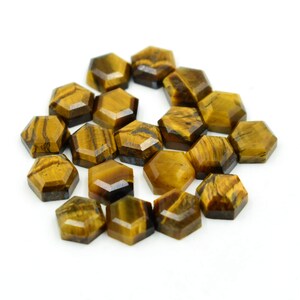 May include: A cluster of hexagonal tiger's eye gemstones. The stones are a warm, golden-brown colour with dark brown stripes and patterns. The gemstones are arranged on a white surface.