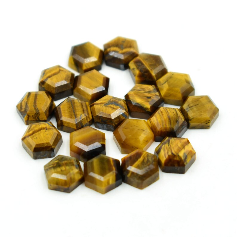 May include: A cluster of hexagonal tiger's eye gemstones. The stones are a warm, golden-brown colour with dark brown stripes and patterns. The gemstones are arranged on a white surface.