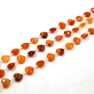 May include: Three strands of faceted heart-shaped carnelian beads in varying shades of orange and deep red. Each bead is strung on a thin silver-colored wire, creating a delicate and uniform arrangement of small, polished gemstone hearts.