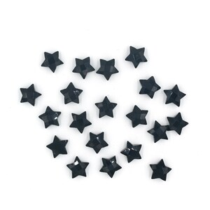May include: A scattering of black star-shaped rhinestones on a white background.