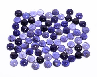 May include: A collection of round, polished gemstones in varying shades of blue and purple. The gemstones are scattered across a white surface, showcasing their smooth, domed surfaces and translucent quality. The gems appear to be cabochons, suitable for jewelry making.