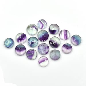 May include: A collection of 15 round, cabochon fluorite gemstones. The stones are a mix of purple, blue, and white colors with a variety of patterns.