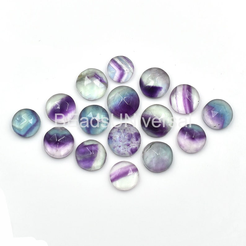 May include: A collection of 15 round, cabochon fluorite gemstones. The stones are a mix of purple, blue, and white colors with a variety of patterns.