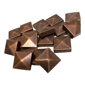 May include: A collection of square, copper-colored decorative studs with a pyramid design on each face. The studs are scattered against a white background, showcasing their metallic finish and geometric shape. These are likely used for upholstery or decorative purposes.