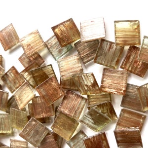May include: A pile of small, square, iridescent glass tiles in shades of brown and gold. The tiles have a metallic sheen and a textured surface.