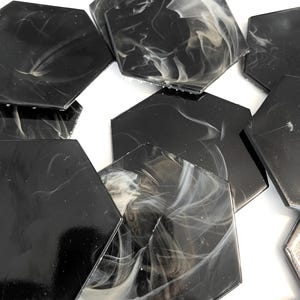 May include: A collection of black hexagonal tiles with a glossy finish. Each tile features a unique swirling pattern of white and gray, creating a marbled effect. The tiles are arranged on a white surface.