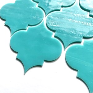May include: A collection of turquoise-colored, quatrefoil-shaped tiles. The tiles have a glossy finish and a slightly translucent appearance, with subtle variations in color. The design is reminiscent of Moroccan or Mediterranean decor.