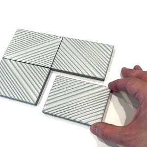 May include: Four white ceramic tiles with a diagonal striped pattern. The tiles are arranged in a staggered pattern.