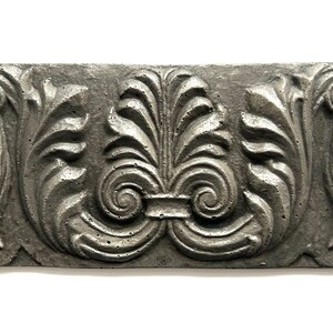 May include: A silver-colored, rectangular, decorative wall tile with a raised, ornate design of stylized leaves and scrolls.