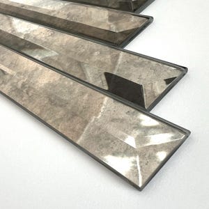 May include: A close-up of a set of rectangular, beveled glass tiles with a light brown, mirrored finish. The tiles are arranged in a staggered pattern, creating a geometric design.