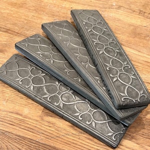 May include: Four gray ceramic tiles with a decorative, embossed, floral pattern. The tiles are arranged in a fan shape.