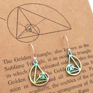 Puede incluir: Pendientes de plata con un diseño geométrico, con forma de triángulo con un diseño interior más pequeño. Los pendientes se muestran en una tarjeta marrón con el texto "Molecular Motifs Inspired by The Universe."