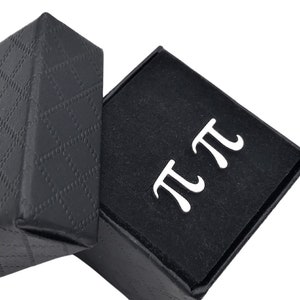 May include: A black gift box with a diamond pattern on the lid is open, revealing a black velvet interior with the Greek letter pi printed in white.