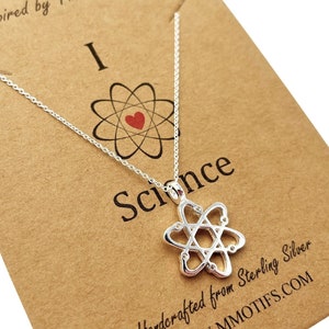 May include: A silver necklace with an atom pendant and the words "I love Science" on a brown card. The card also says "Molecular Motifs Inspired by The Universe" and "Handcrafted from Sterling Silver" with the website address "www.mmotifs.com".