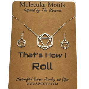 May include: A silver necklace and earrings set featuring a geometric, 3D, dice-shaped pendant and matching earrings. The card reads "Molecular Motifs Inspired by The Universe That's How I Roll Handcrafted Science Jewellery and Gifts WWW.MMOTIFS.COM".