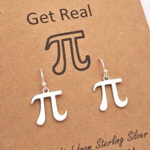 Puede incluir: Un par de pendientes de plata de ley en forma del símbolo matemático pi. Los pendientes están en una tarjeta marrón con el texto "Get Real" y un símbolo pi más grande.