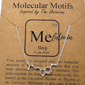 May include: A silver-colored necklace featuring the molecular structure of melatonin, displayed on a brown card. The card reads "Melatonin Sleep" and includes the chemical formula. The card also has the text "Molecular Motifs Inspired by The Universe."